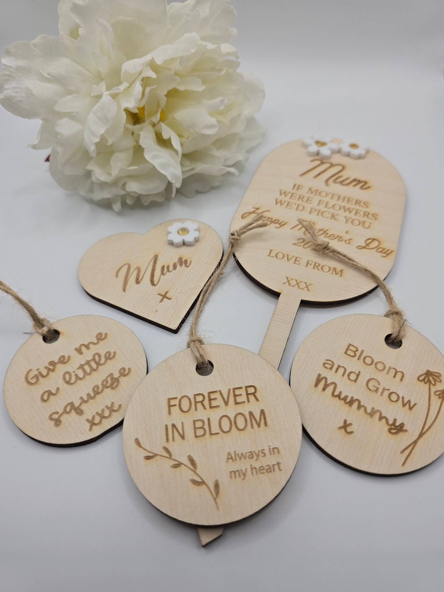 Wooden tags with engraved messages and a white flower on a light gray background