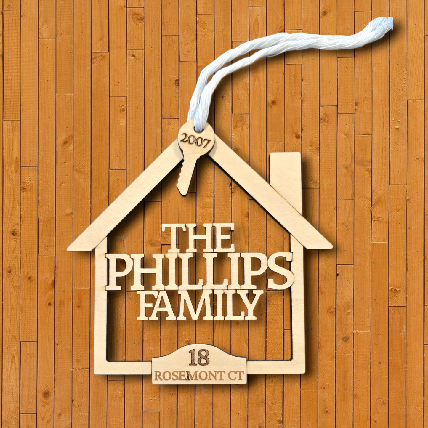 Wooden house-shaped sign with 'The Phillips Family' and address on a wooden background