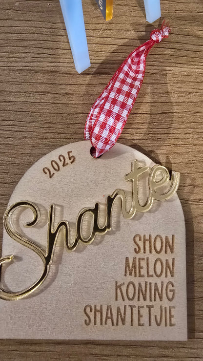 Decorative wooden ornament with 'Shante' and '2025' text, hanging on a wooden surface.