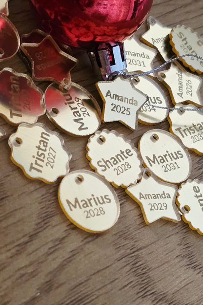 Collection of personalized name tags on a wooden surface with a red ornament in the background.