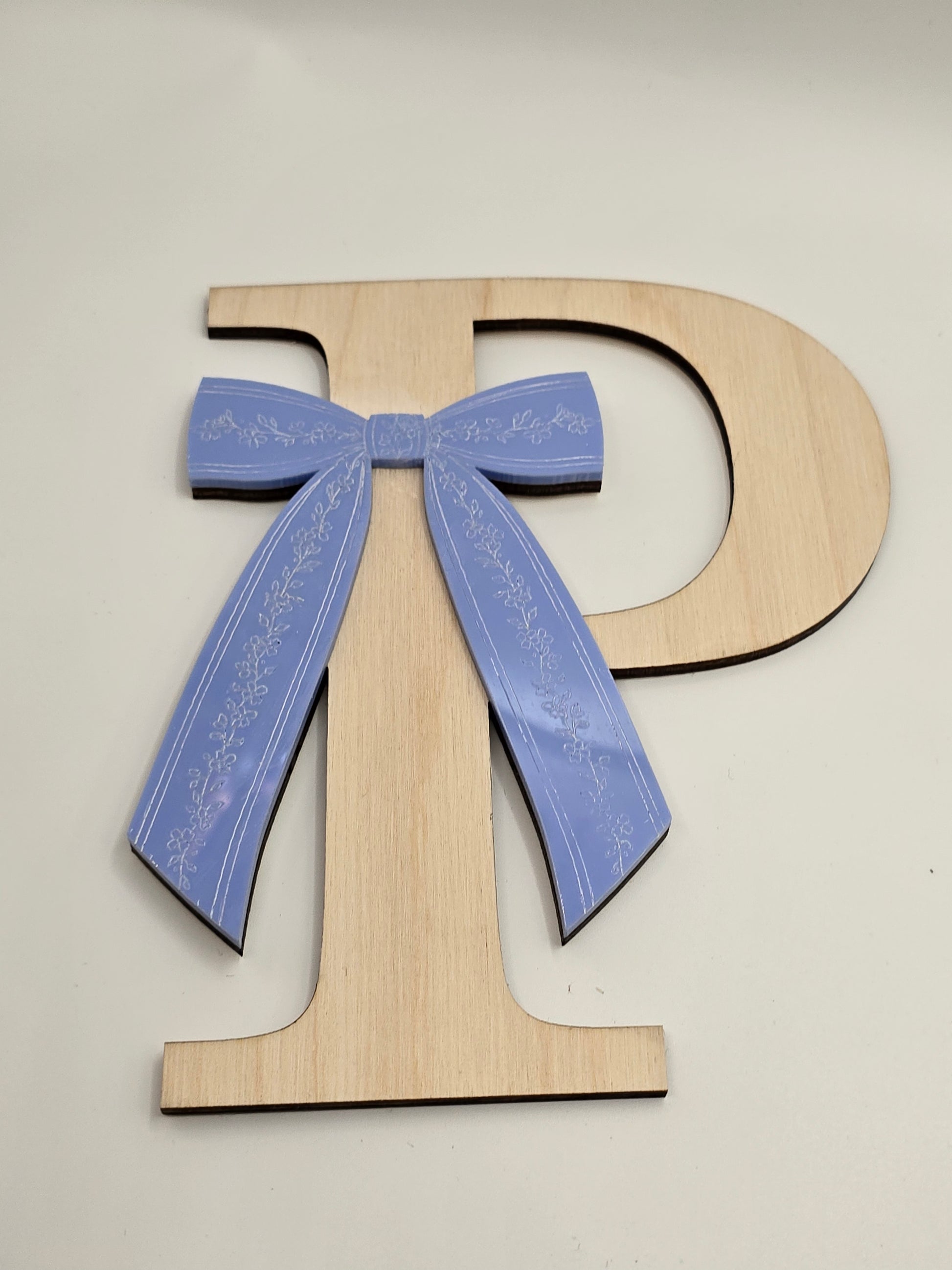 Wooden letter 'D' with a blue bow on a white background