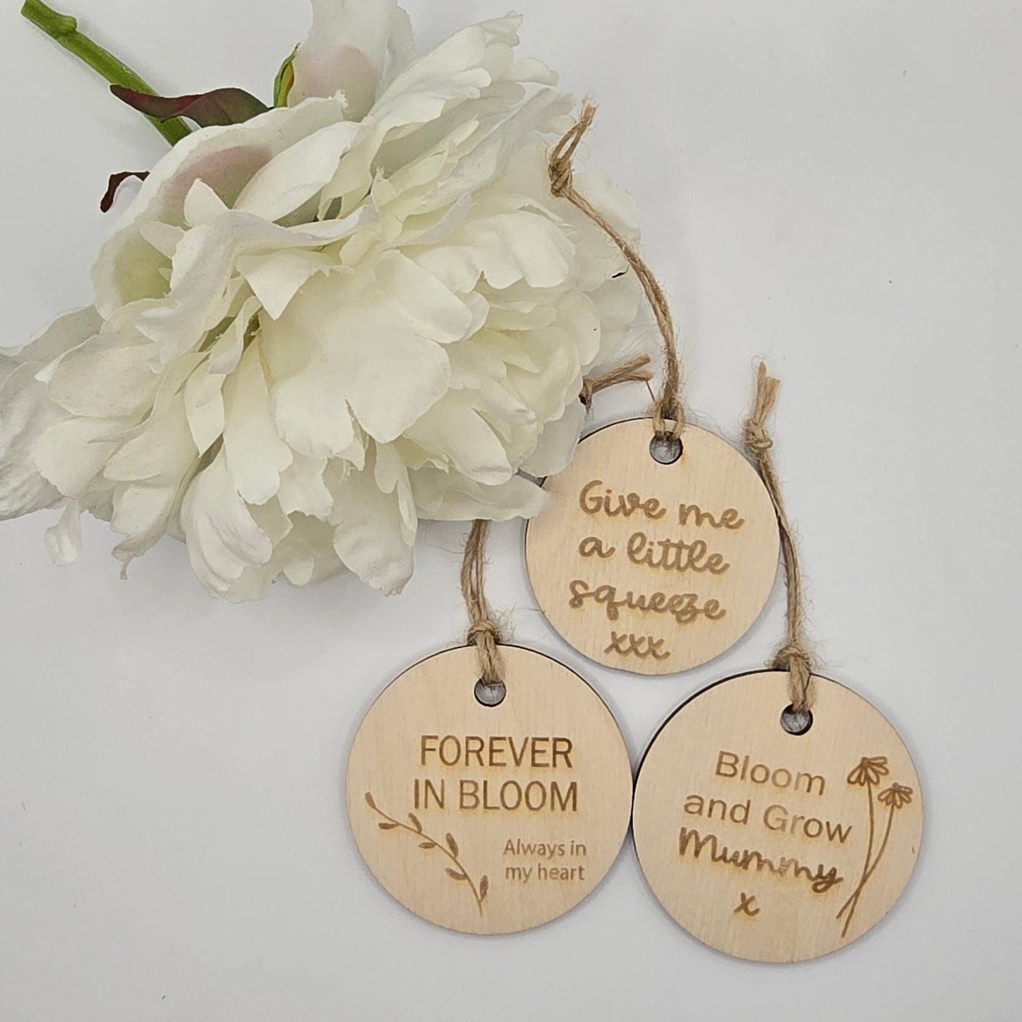 Three wooden tags with engraved text and a white flower on a light gray background