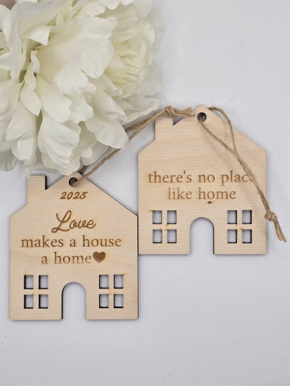Two wooden house-shaped tags with engraved text on a white background with white flowers.