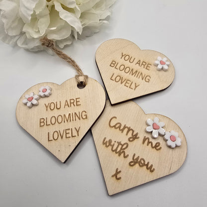 Three wooden heart-shaped tags with floral designs and text on a light background