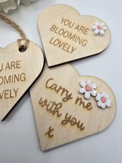 Three wooden heart-shaped tags with floral designs and engraved text on a light background.