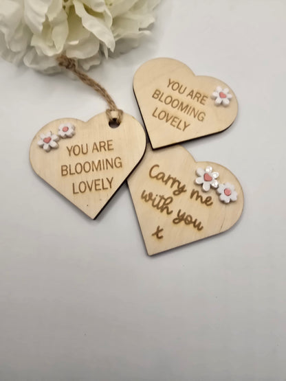 Three wooden heart-shaped tags with floral designs and text on a light background