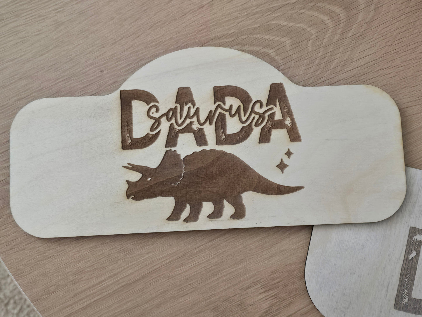 Wooden sign with 'DADASaurus' and a triceratops design on a wooden surface