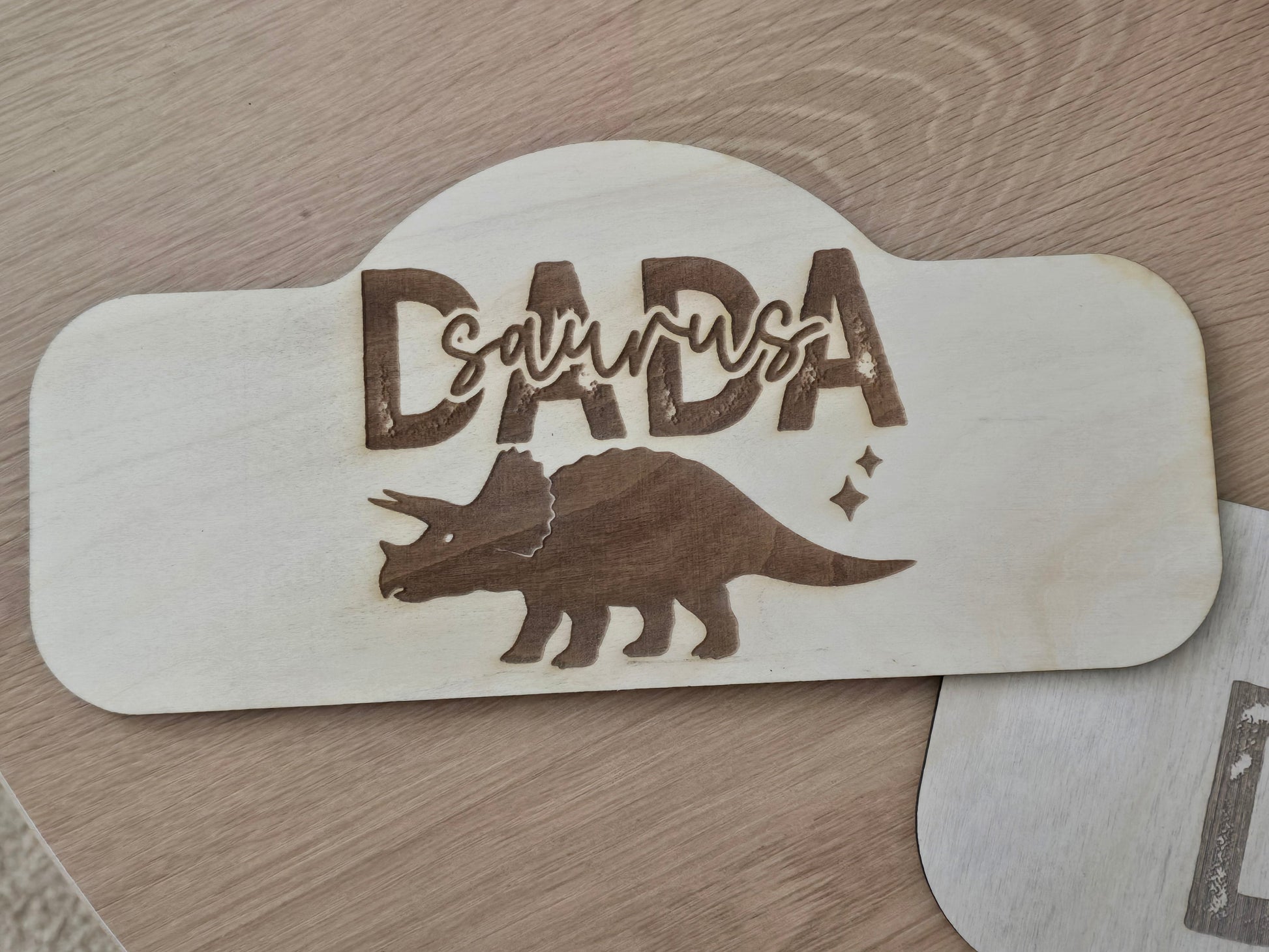 Wooden sign with 'DADASaurus' and a triceratops design on a wooden surface