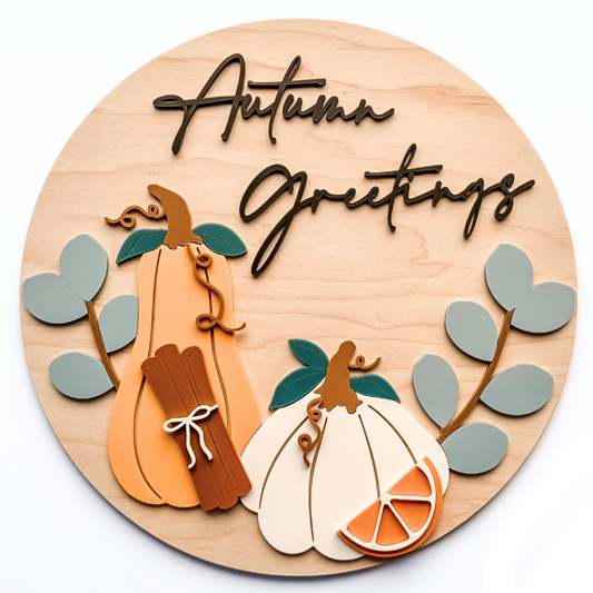 Wooden circular decoration with pumpkins and autumn leaves, featuring the text 'Autumn Greetings'.