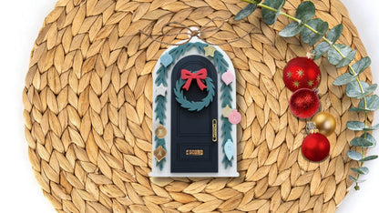 Decorative door ornament with wreath and bow on a woven mat with Christmas decorations.