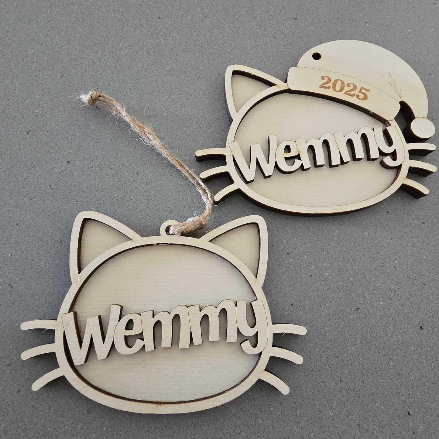 Two cat-shaped ornaments with 'Wemmy' engraved on a gray background