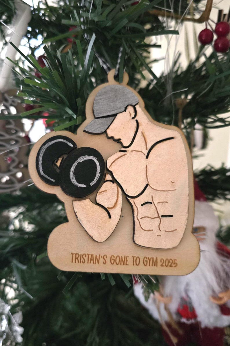 Wooden ornament of a man lifting weights with 'Tristan's Gone to Gym 2025' text on a Christmas tree.