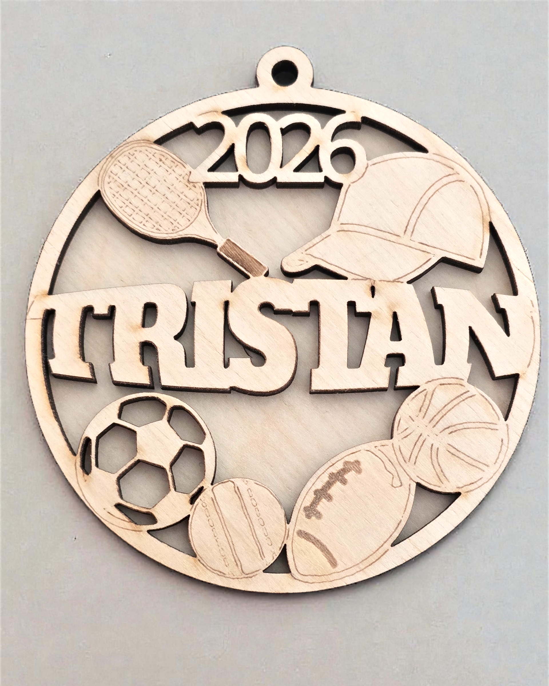 Decorative metal ornament with sports-themed elements and '2026 Tristan' text on a gray background