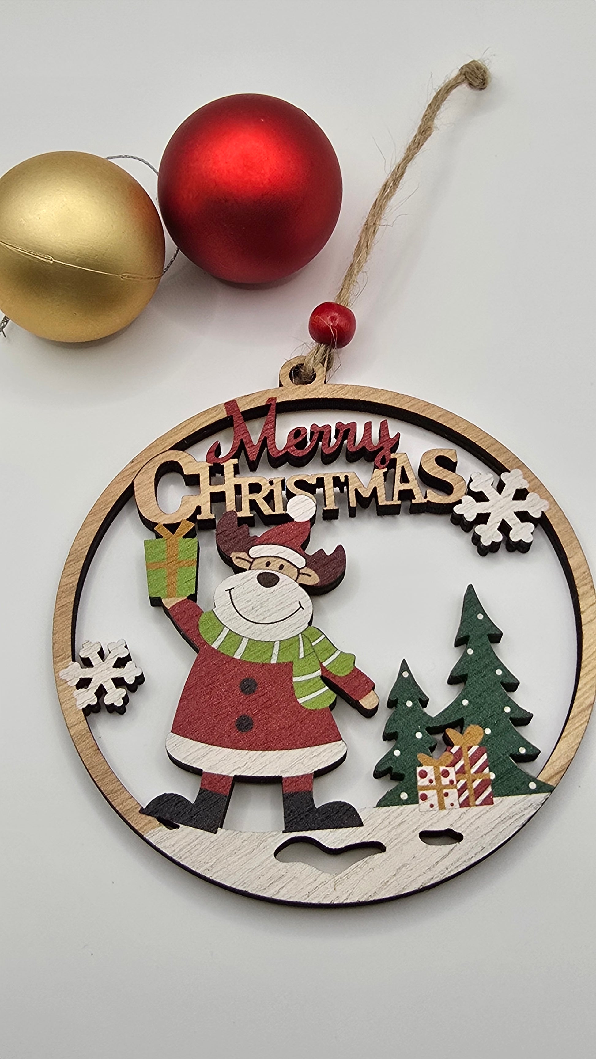 Wooden Christmas ornament with Santa Claus design and 'Merry Christmas' text, surrounded by red and gold baubles on a light gray background.