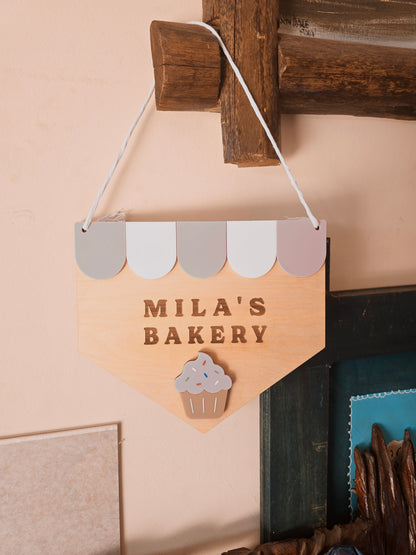 Custom wooden “Name’s Bakery” kids playroom sign by PeppaTree Designs, featuring colorful painted lettering on natural wood background.