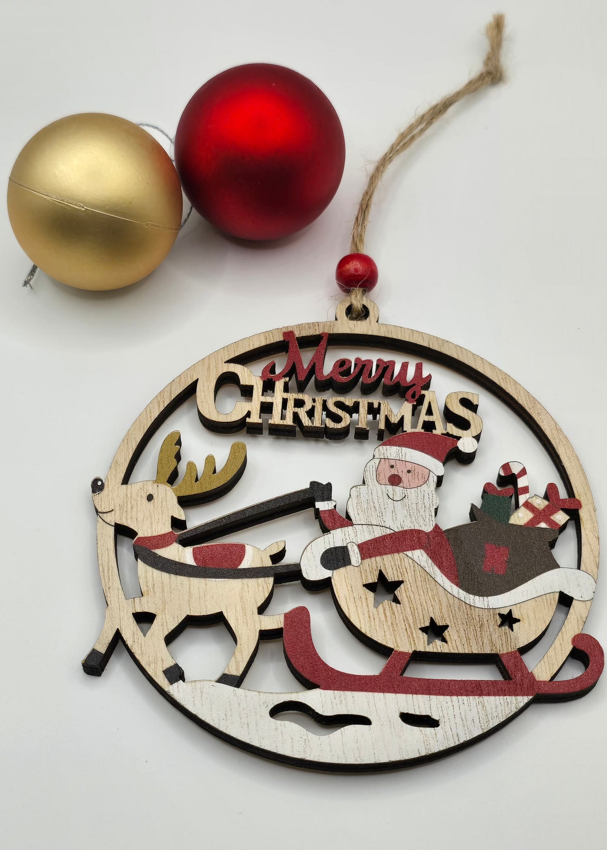 Wooden Christmas ornament with Santa Claus and reindeer design, accompanied by gold and red baubles on a white background.