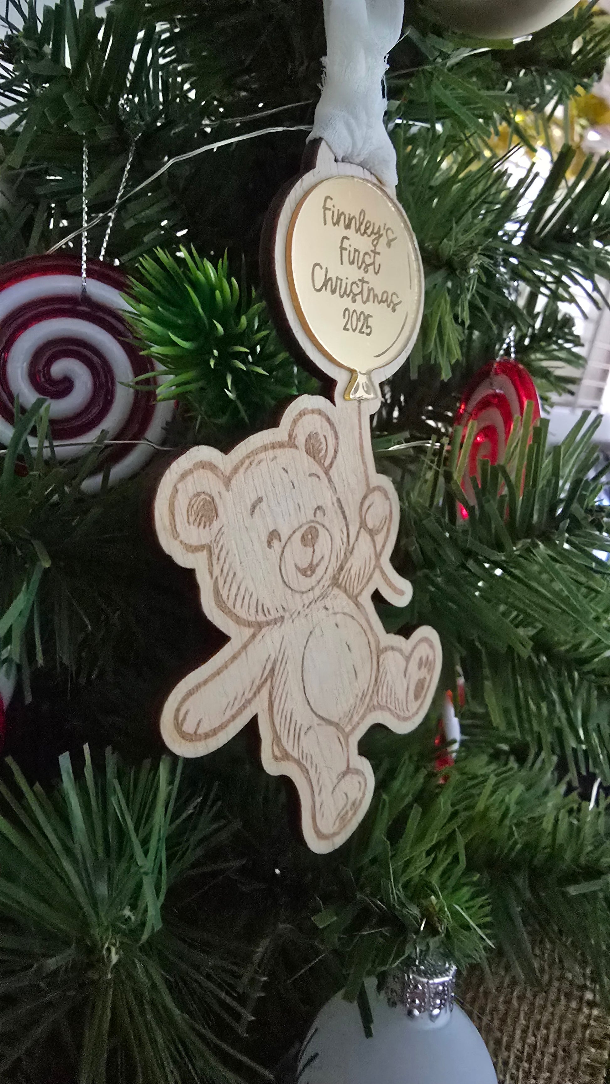 Wooden teddy bear ornament with 'First Christmas' text on a decorated tree.