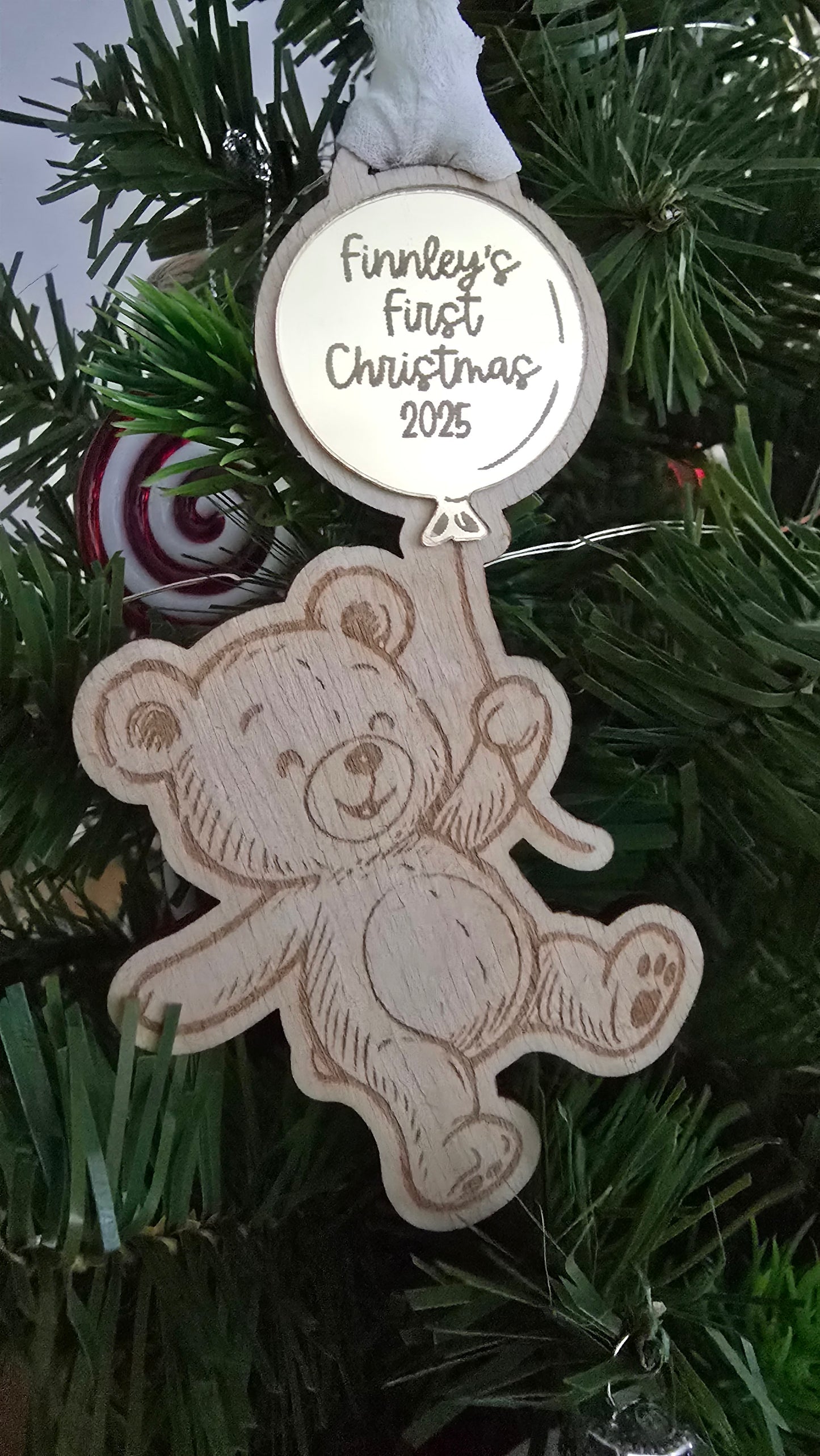 Decorative ornament with teddy bear design and 'Finnley's First Christmas 2023' text on a Christmas tree.